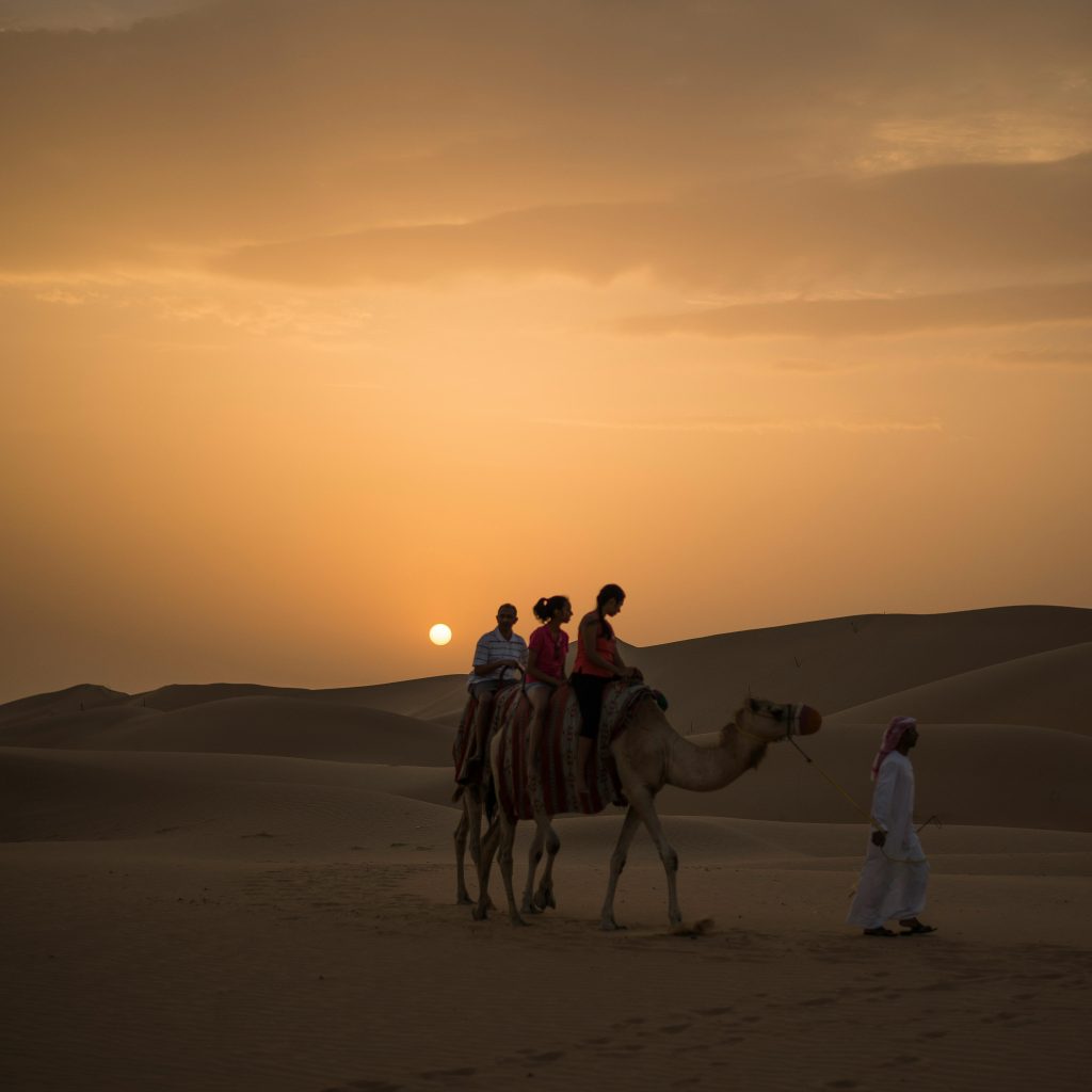 Tourists riding camels across Dubai’s desert dunes during a budget-friendly safari – an affordable adventure included in budget travel tips Dubai tours.